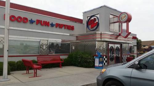 Exterior of a retro-style diner with a red and silver facade, featuring a large sign and a bench outside.