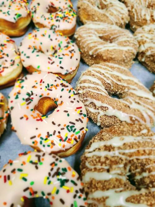A variety of donuts: some with pink icing and sprinkles, others coated in cinnamon sugar and drizzled with icing.
