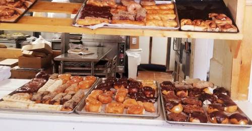 Trays of assorted pastries and donuts, some topped with chocolate, displayed in a bakery.