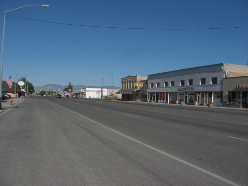 A quiet street in a small town, featuring storefronts and clear blue skies in the background.