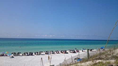 A sunny beach scene with umbrellas and chairs on white sand, turquoise water, and a clear blue sky.