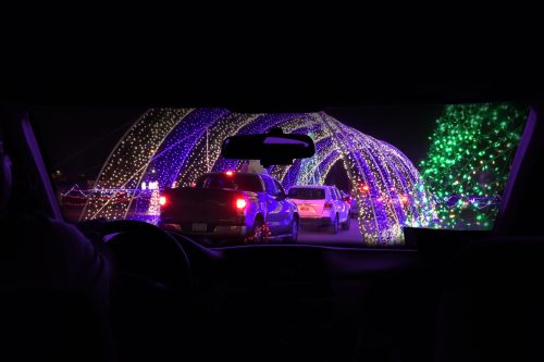 View from inside a car showing a colorful light display with vehicles lined up under illuminated arches.