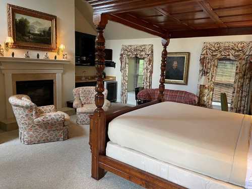 A cozy room featuring a four-poster bed, armchairs, a fireplace, and decorative curtains.