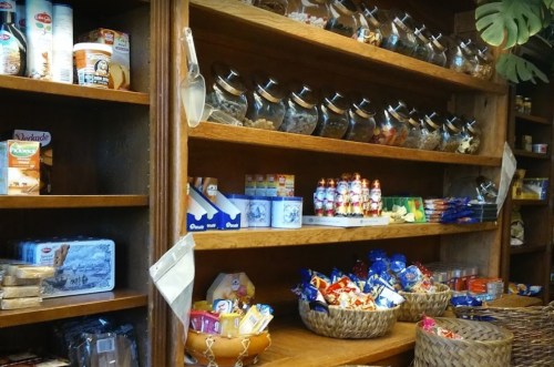 A wooden shelf filled with jars of snacks, packaged goods, and baskets of treats in a cozy store setting.