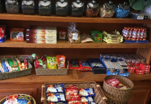 A wooden shelf filled with various snacks, candies, and packaged goods in baskets and jars.