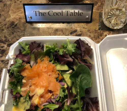 A salad with mixed greens and salmon, next to a sign reading "The Cool Table" on a marble surface.