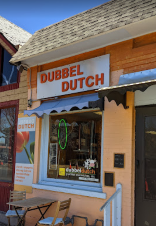 A storefront with an orange exterior and a sign reading "Dubbel Dutch," featuring outdoor seating and a blue sky.