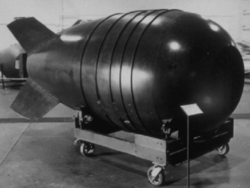 A large, cylindrical bomb on a wheeled cart, displayed in a museum setting.