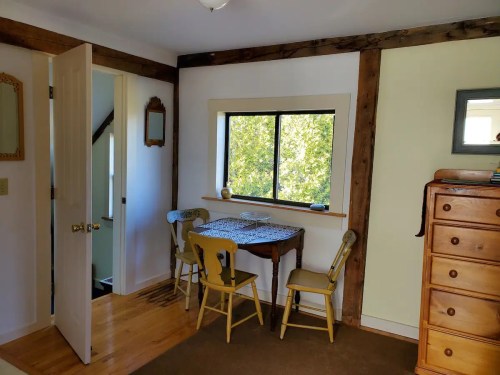 Cozy room with a wooden table and chairs, a window with greenery outside, and a dresser against the wall.