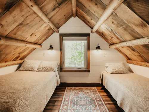 Cozy attic bedroom with two beds, wooden beams, and a window overlooking greenery. Warm, inviting decor.