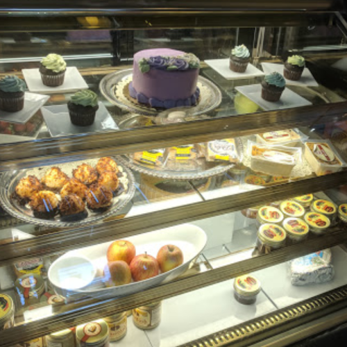 A display case filled with cupcakes, a purple cake, pastries, apples, and various desserts.