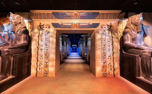 A grand hallway with ancient Egyptian statues and hieroglyphics, leading to a blue-lit area.