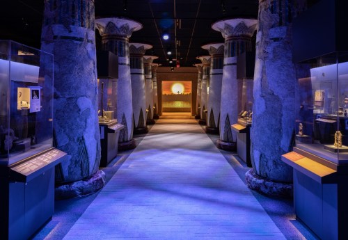 A dimly lit museum corridor with tall, decorative columns and display cases showcasing artifacts.