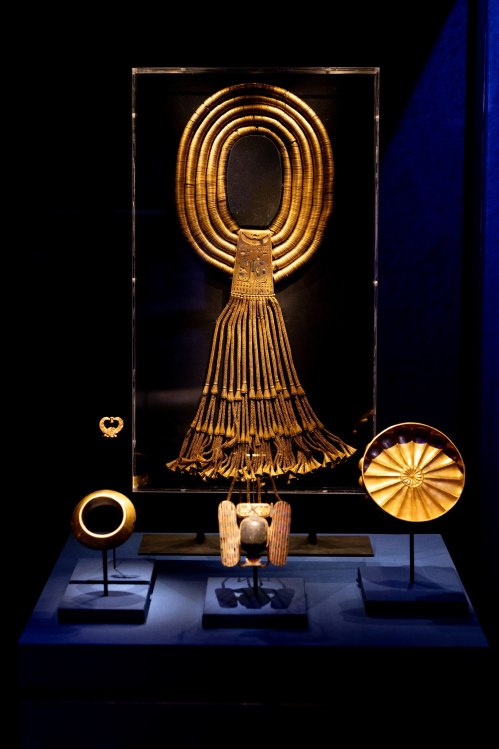 Display of ancient gold jewelry, including a headdress and decorative pieces, showcased under soft lighting.