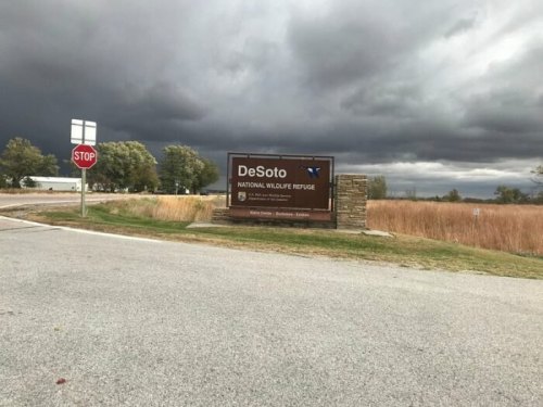 Sign for DeSoto National Wildlife Refuge with dark storm clouds in the background and a stop sign nearby.