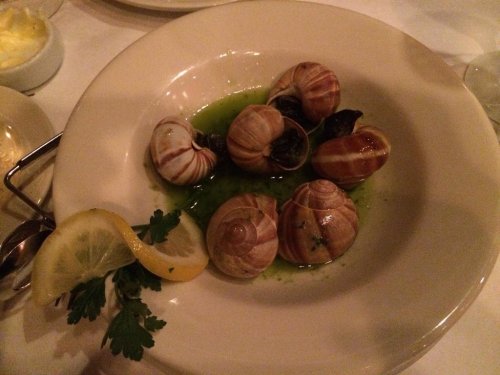 A plate of escargot in green sauce, garnished with a lemon wedge and parsley.