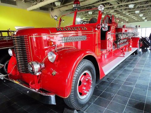 A vintage red fire truck displayed indoors, featuring chrome details and a shiny finish.