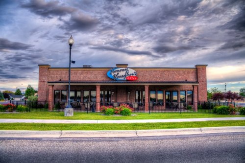 Exterior view of Tommy Vaughan's restaurant, featuring a brick facade and colorful landscaping under a cloudy sky.