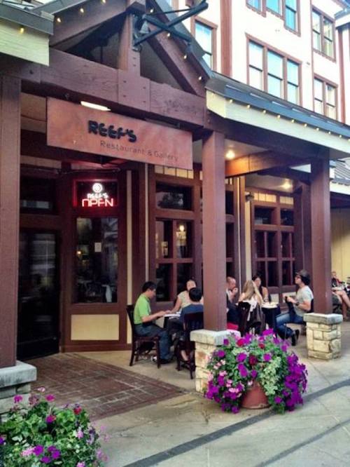 Exterior of Reef's Restaurant & Gallery with outdoor seating and colorful flower pots. People dining at tables.