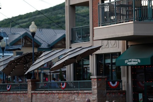 A restaurant with outdoor seating and umbrellas, decorated with red, white, and blue bunting, in a lively area.