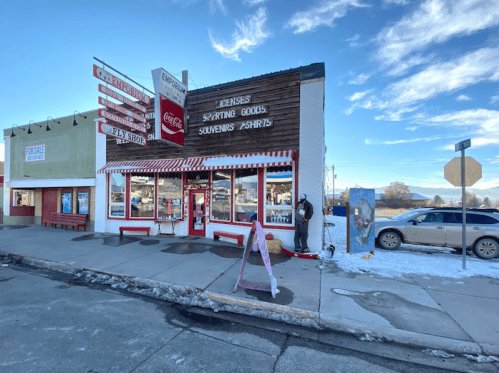 A quaint storefront with signs for souvenirs and gifts, surrounded by snow and a clear blue sky.