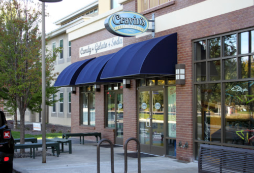 Exterior of Cravin's, a candy, gelato, and soda shop, featuring blue awnings and large glass windows.