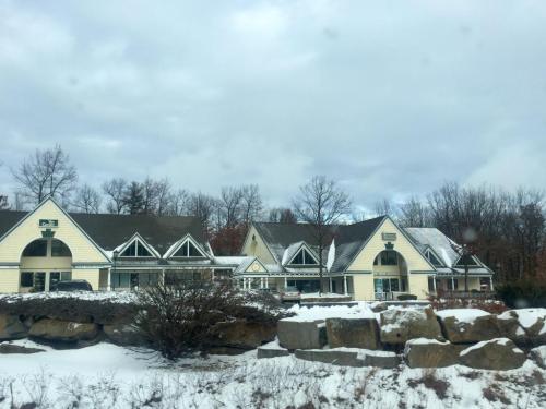 A snowy landscape featuring a large, yellow building with multiple gabled roofs and surrounding trees.