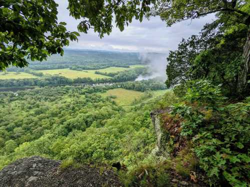 A scenic view from a rocky overlook, showcasing lush green valleys and a river shrouded in mist.