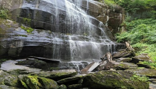 A serene waterfall cascading over rocky cliffs, surrounded by lush greenery and moss-covered stones.