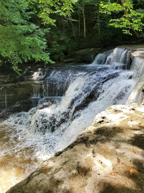 A serene waterfall cascading over rocks, surrounded by lush green trees and sunlight filtering through the leaves.
