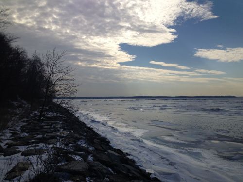 A serene winter landscape featuring a frozen river, rocky shoreline, and cloudy sky.