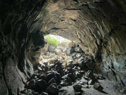 A dark cave entrance with scattered rocks and bright light shining through from outside.