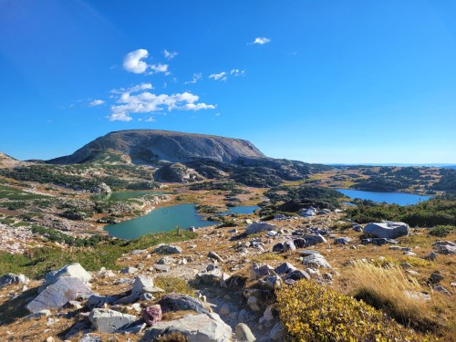 A scenic landscape featuring rolling hills, clear blue lakes, and a bright blue sky with a few clouds.