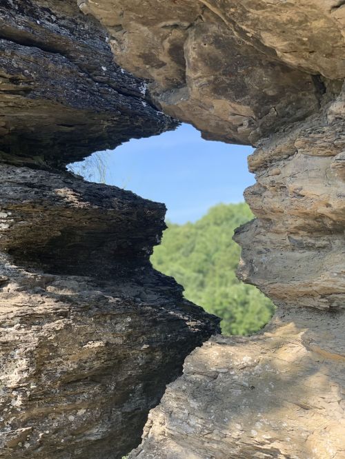 A natural rock formation with a hole, framing a view of green hills and a clear blue sky.