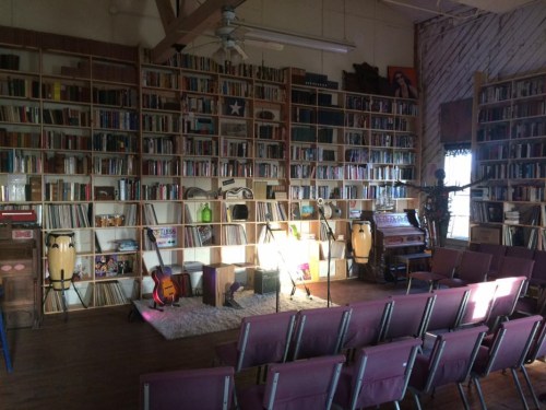 A cozy room with a large bookshelf, musical instruments, and chairs arranged for a performance.