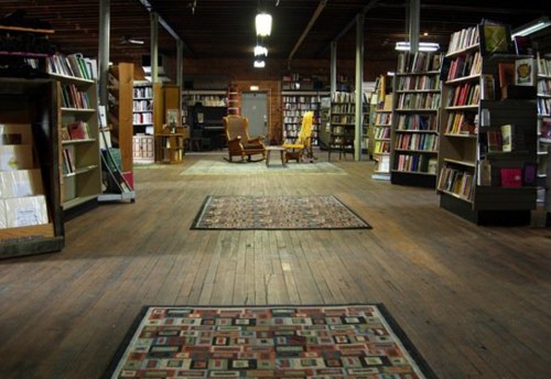 A cozy bookstore interior with wooden floors, bookshelves, and two armchairs in the center.