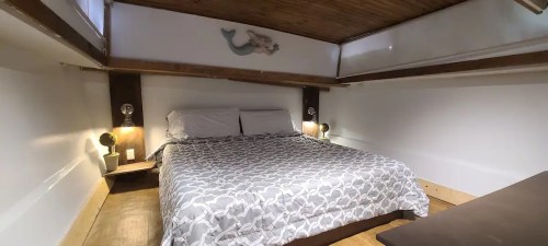 Cozy bedroom with a double bed, wooden ceiling, and decorative mermaid artwork on the wall.