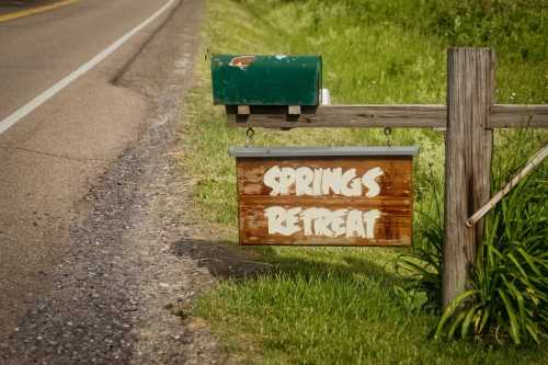 A wooden sign reading "Springs Retreat" hangs from a post near a roadside mailbox, surrounded by green grass.