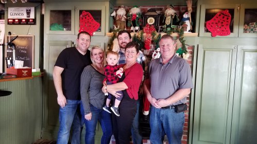 A group of six people, including a baby, pose together in a festive setting with holiday decorations.