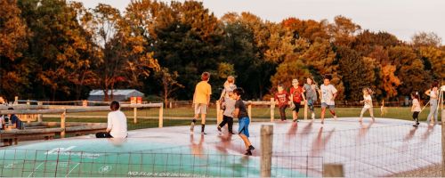 Children playing on a large inflatable bounce pad in a park during sunset, surrounded by trees.