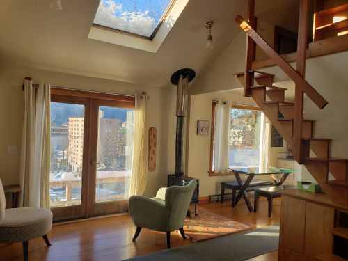 Cozy interior with a skylight, wooden stairs, and a view of a cityscape through large windows.