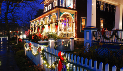 A beautifully decorated house with festive lights and wreaths, surrounded by a white picket fence and holiday decorations.