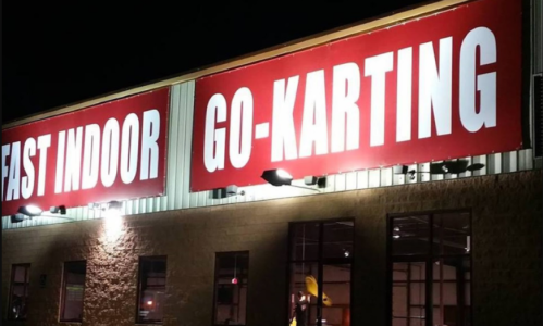 Bright red signs on a building read "EAST INDOOR GO-KARTING" at night, illuminated by exterior lights.
