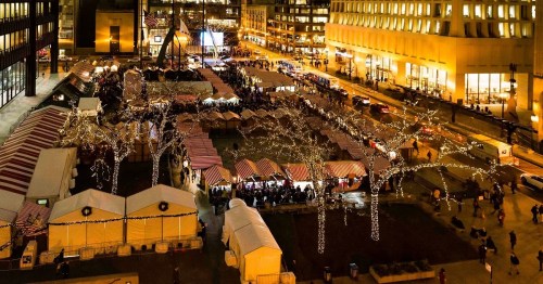 Aerial view of a festive market with illuminated stalls and trees, bustling with people at night.