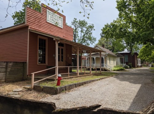 Historic building with a porch, surrounded by trees, and a fire hydrant in a quiet, gravel-lined street.