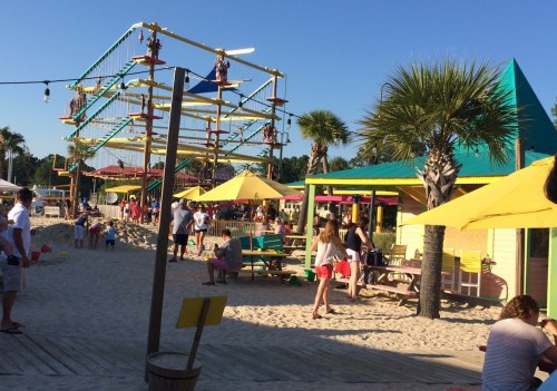 A vibrant beach area with colorful umbrellas, palm trees, and people enjoying various activities in the sand.