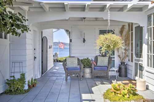 Cozy outdoor seating area with potted plants, overlooking a serene water view and American flags in the background.