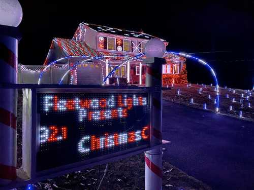 A house decorated with colorful Christmas lights, featuring a digital sign displaying "Flawed Lights 2021."