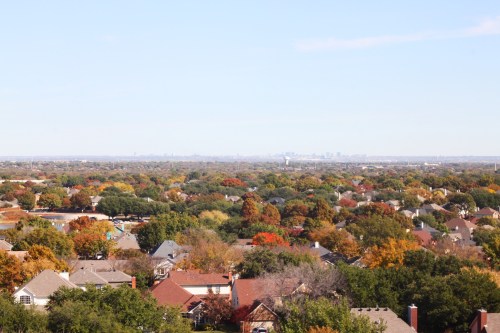 A panoramic view of a suburban landscape with colorful autumn trees and a distant city skyline under a clear blue sky.