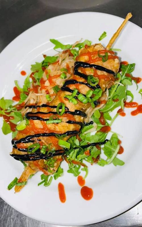 A plate of skewered fried food drizzled with sauce, garnished with green onions and served on a bed of salad.